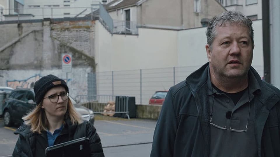 On the left is a smaller blond woman with a hat. On the right old man, rather broad. walking in the street