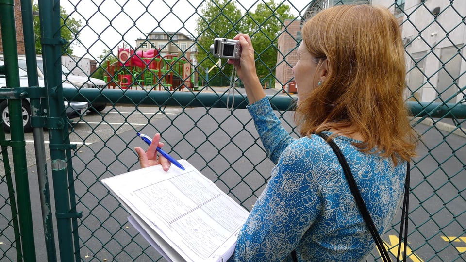 Eine Frau fotografiert hinter einem Zaun.