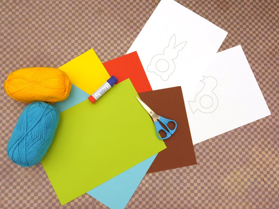 Auf diesem Bild sehen Sie die Vorlage zum Ausdrucken, eine Schere, einen Leimstift, farbige Wolle und dickes farbiges Papier.