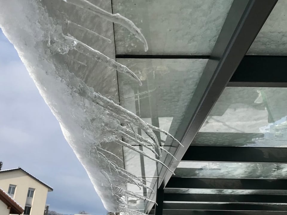 Eiszapfen an Schnee, der von einem Glasdach rutscht.