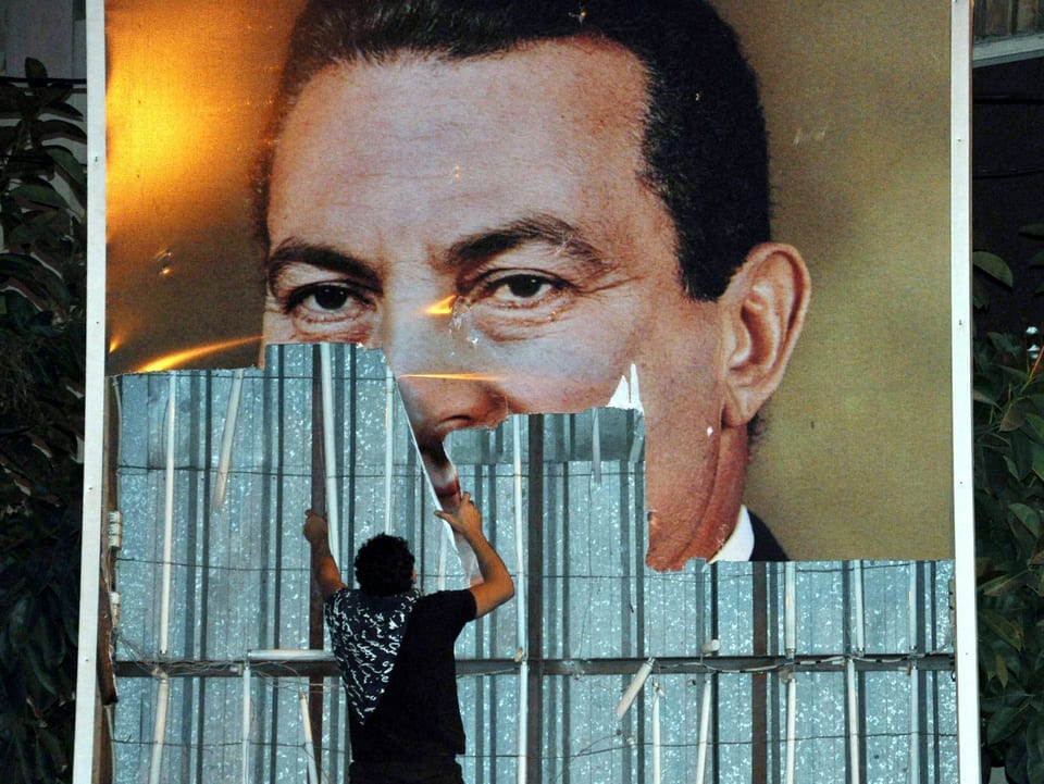 Ein Ägyptischer Demonstrant reist ein Poster des ehemaligen Präsidenten Hosni Mubarak herunter.