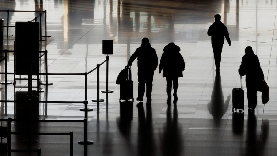 Vier Menschen laufen mit Koffern in einer Flughafenhalle. Es sieht so aus, als hätte es nicht viele Leute am Flughafen.