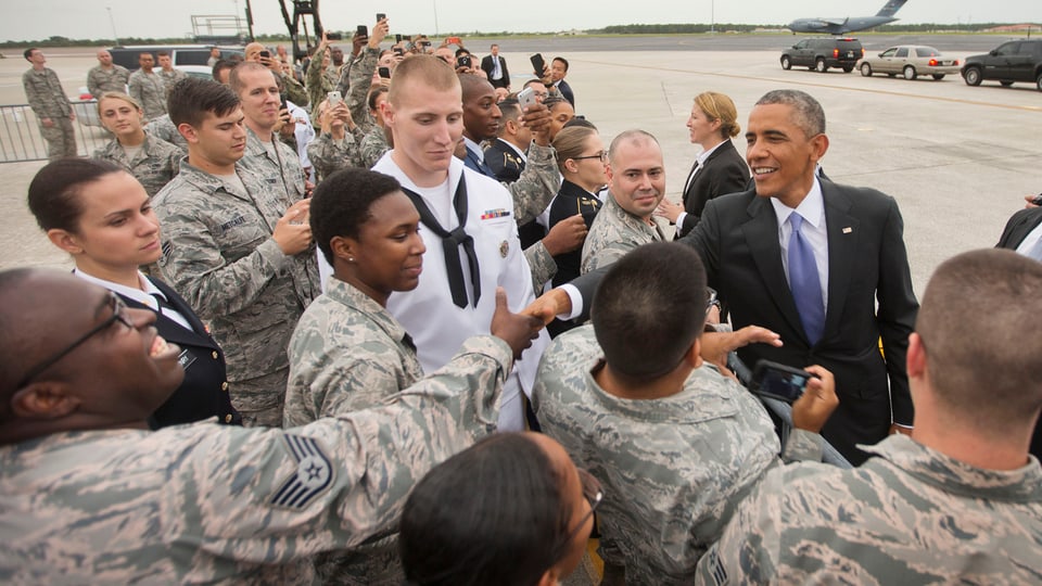 Obama schüttelt auf einem Flugplatz die Hände von Armeeangehörigen.