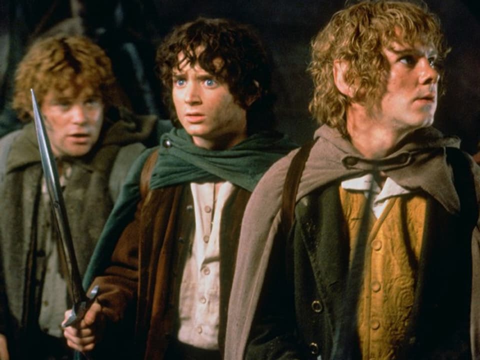 Drei Jungendliche in historischen Kostümen, wobei einer ein Schwert in der Hand hat.
