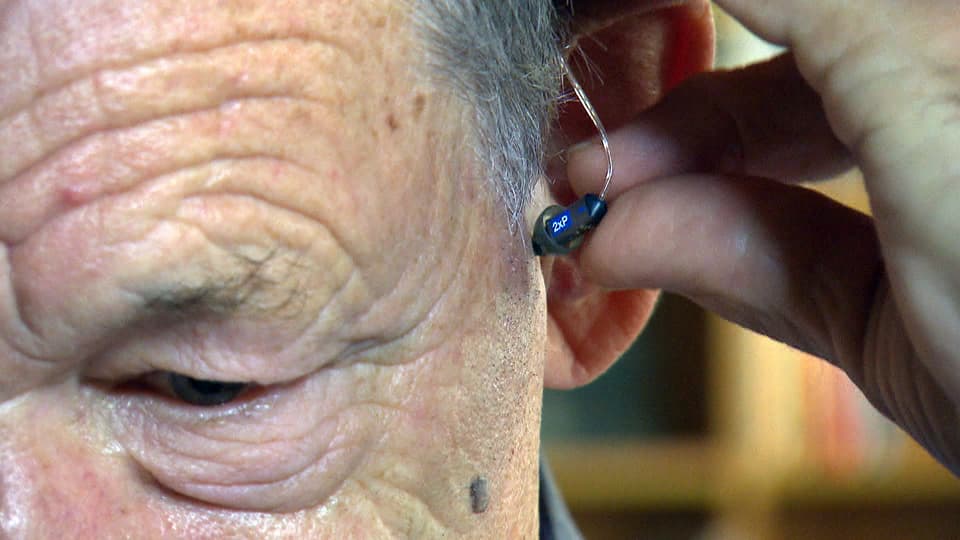 Mann schiebt sich ein Hörgerät ins Ohr.