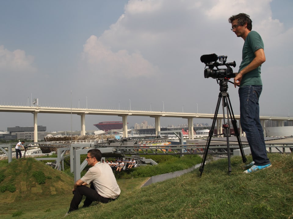 Ein Mann mit Kamera steht auf einem Grashügel. im Hintergrund die Stadt Shanghai.