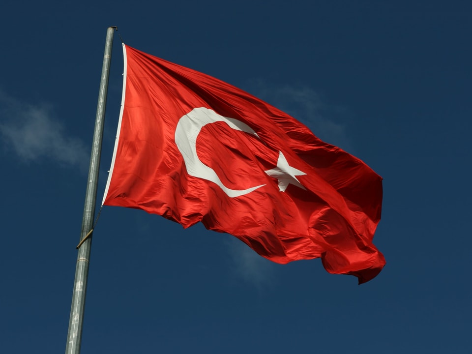 Die türkische Flagge weht vor blauem Himmel.