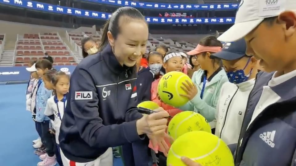 Peng signiert Tennisbälle in einer Halle.