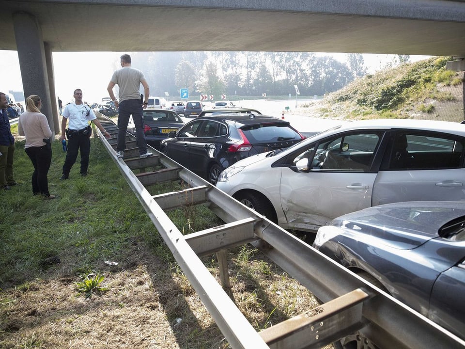 Leute stehen am Rande der Autobahn vor demolierten Autos