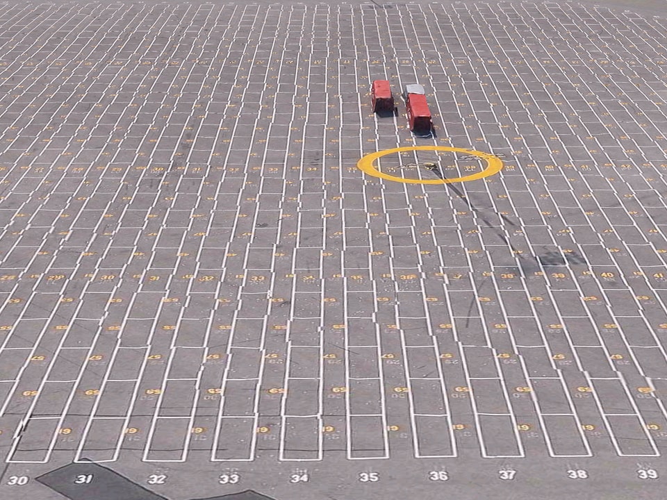 3D-Kartenansicht: Ein riesiger, leerer Parkplatz. Die Linien sind schief, zwei etwas unförmige Container stehen auf dem Platz