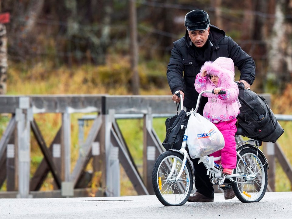 Ein Mann mit einem Kind auf einem Fahrrad überquert eine Brücke.