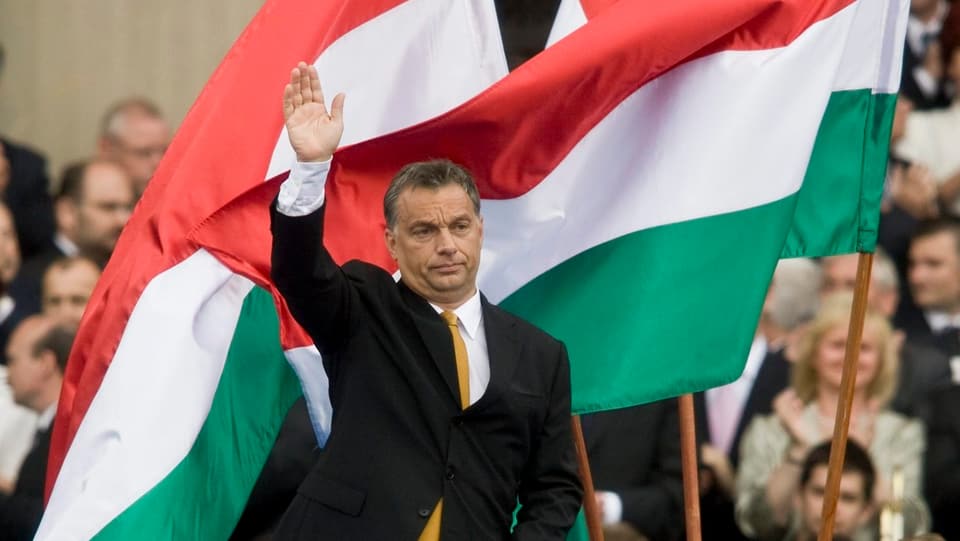 Orban steht vor Fahnen und winkt