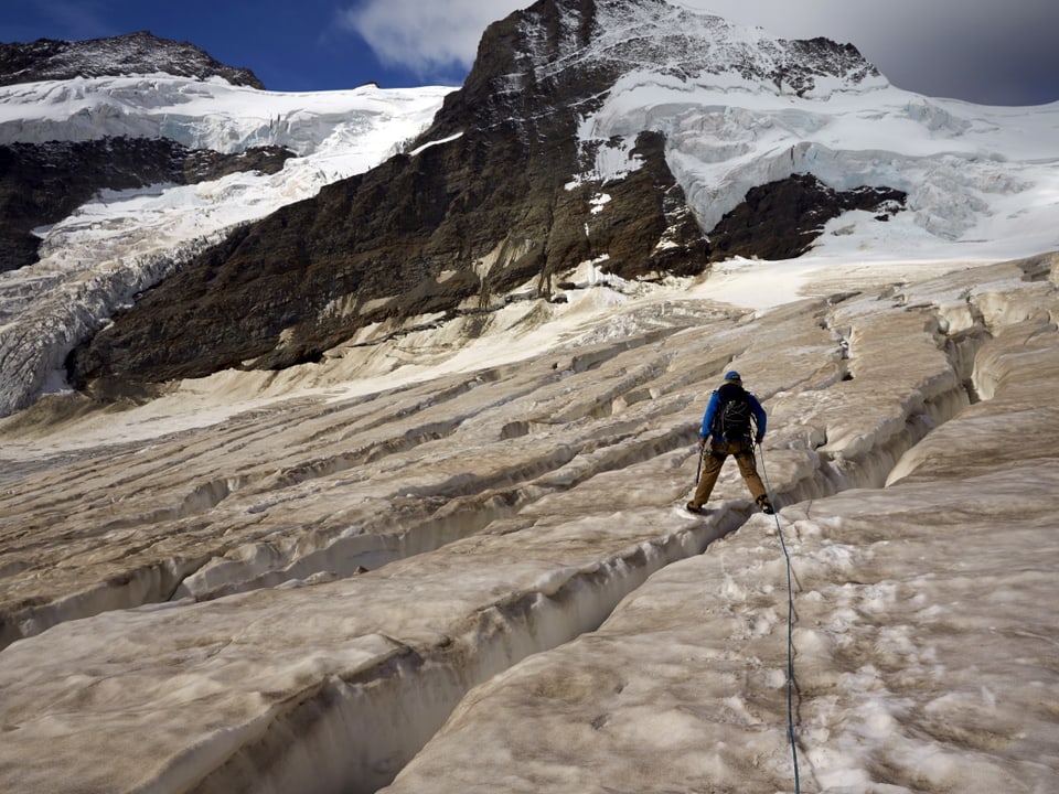 Ein Bergsteiger steht über einer Gletscherspalte, er ist mit einem Seil gesichert.