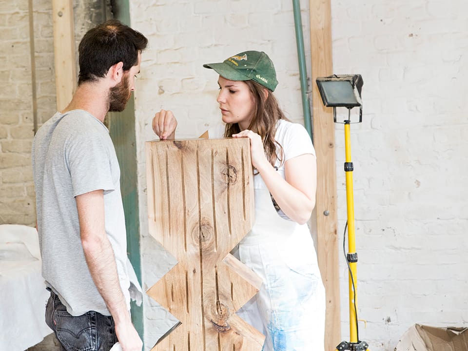Künstlerin Claudia Comte unterhält sich mit einem jungen Mann über eine Holzskulptur, die sie in Händen hält.