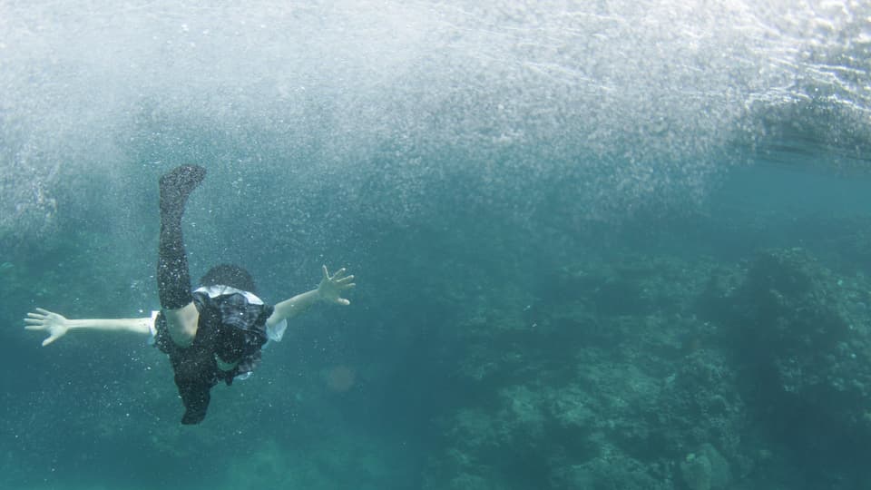 Ein Mädchen schwimmt bekleidet im Meer.