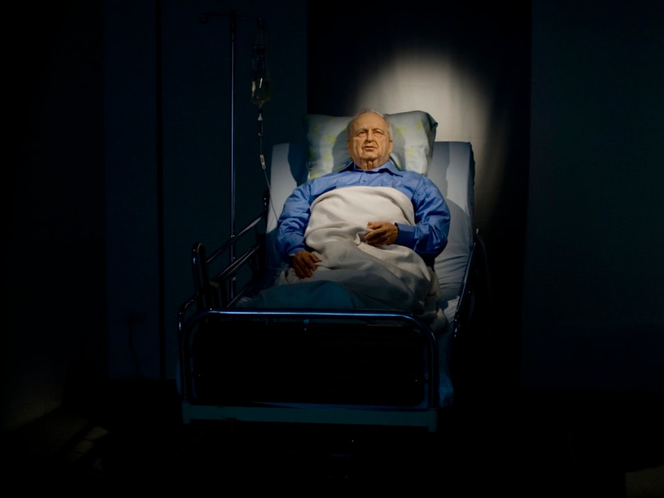 Eine Kunstinstallation zeigt Ariel Sharon in einem Krankenbett liegend.