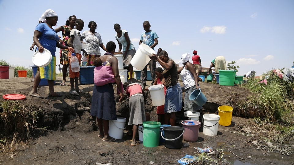 Eine Gruppe von afrikanischen Personen füllt Wasser in Eimer und Behälter ab. 