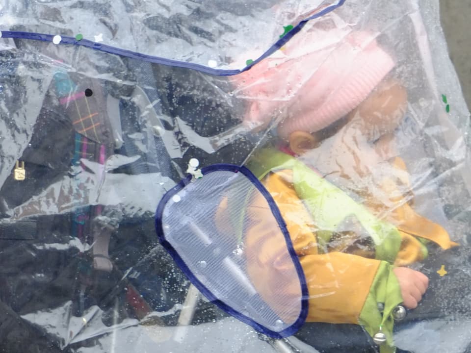Kind hinter Plastikabdeckung im Kinderwagen