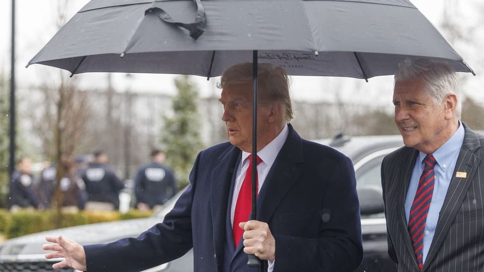 Donald Trump steht unter einem Regenschirm.