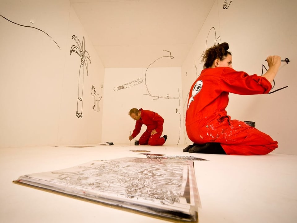 Zwei Personen im roten Overall bemalen Wände in einem weissen Raum