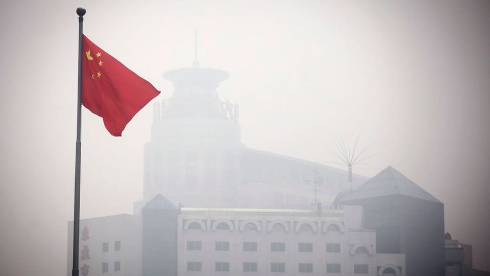 Chinesische Flagge vor einem Gebäude in Peking, das durch den Smog kaum sichtbar ist.