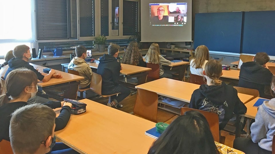 Aufgrund der Corona-Schutzmassnahmen verfolgen die übrigen Schülerinnen und Schüler der 9a und 9b die Videokonferenz in einem separaten Klassenzimmer.