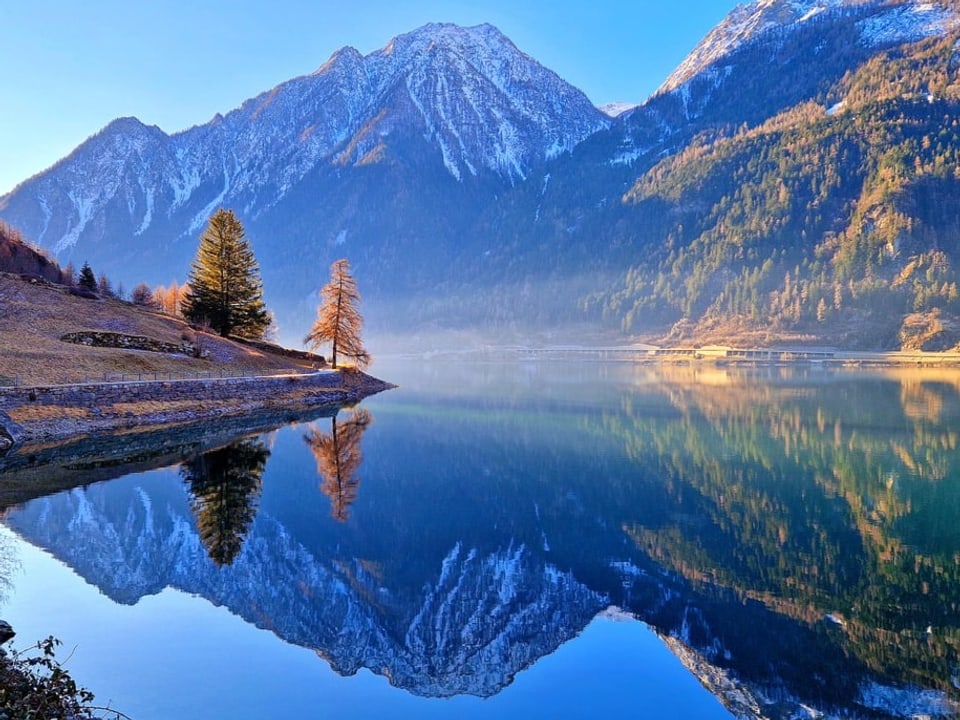 Blick auf Bergsee in der Morgensonne, in dem sich die umliegenden angezuckerten Berge spiegeln. 