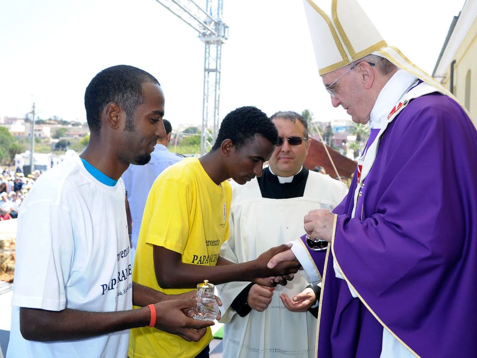 Der Papst gibt Flüchtlingen die Hand.
