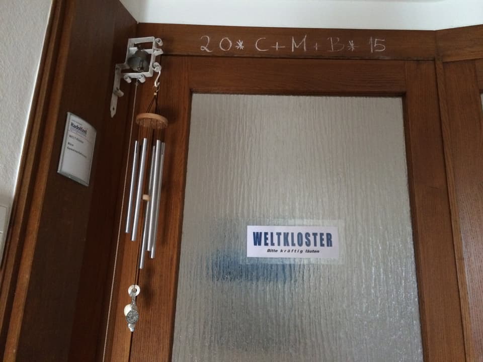 Vor der Eingangstür hängt ein Klangspiel. An der Glastüre hängt ein Schild mit der Aufschrift «Weltkloster – bitte kräftig läuten».