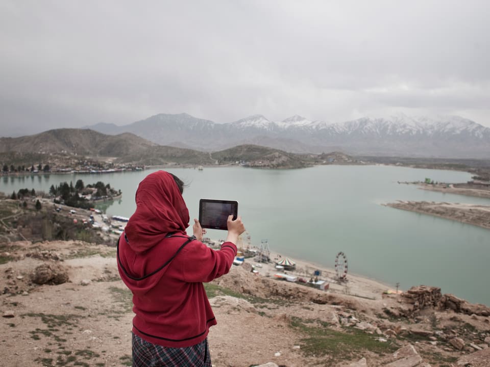 Eine Frau mit einer roten Jacke macht mit einem Tablet ein Foto eines Sees.
