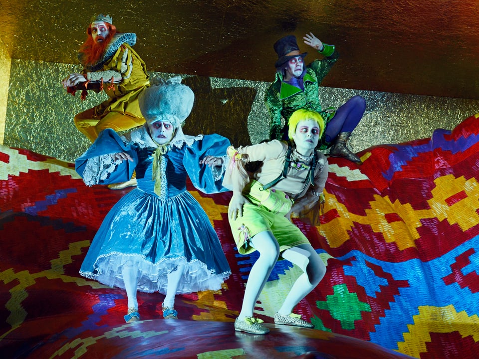 Vier Schauspieler in bunten Kostümen, mit weisser Schminke und roten umrandeten Augen.