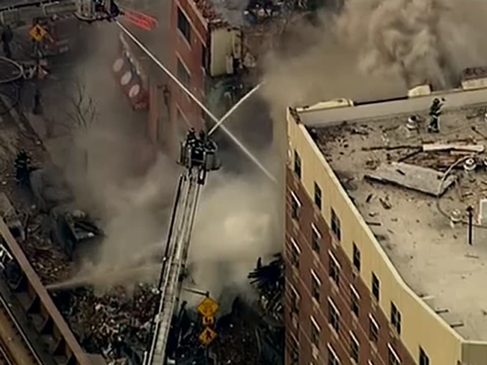 Feuerwehrmänner spritzen von Leitern aus Wasser auf die zestörten Gebäude