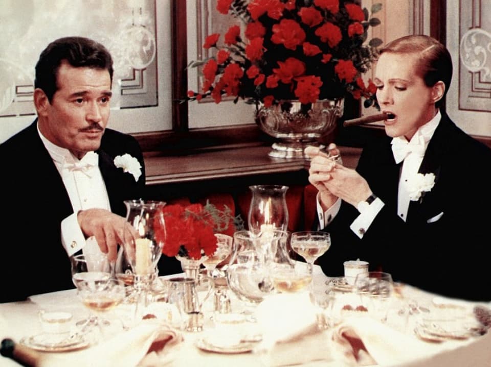 Ein Mann und eine Frau sitzen in einem Smoking an enem Tisch eines eleganten Restaurants.