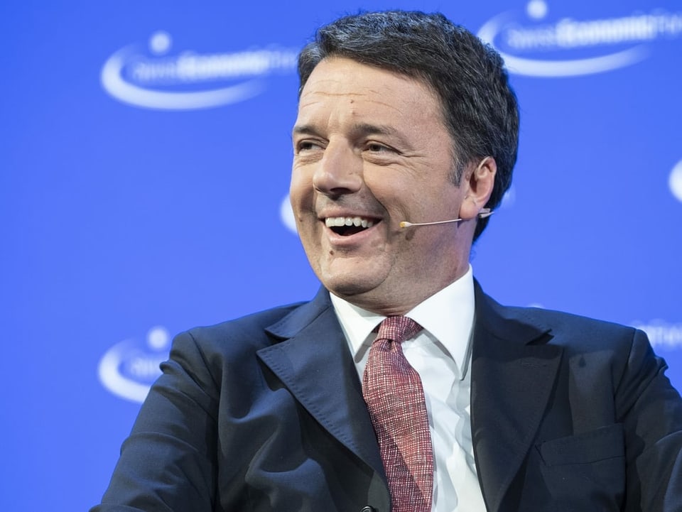 Matteo Renzi sitzt auf einer Bühne. Er lacht.