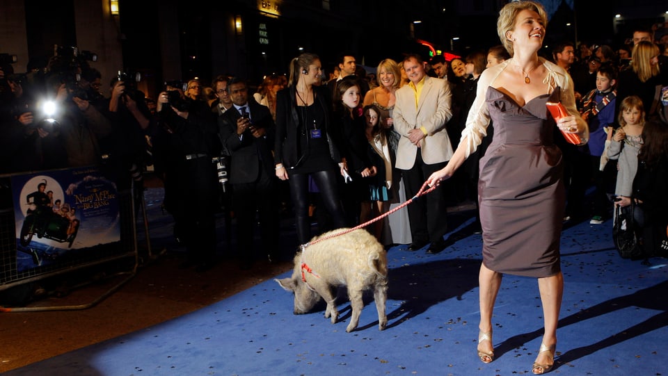 Emma Thompson steht auf einem blauen Teppich. An der Leine führt sie das weisse Schwein, im Hintergrund tummeln sich Fans und Fotografen.