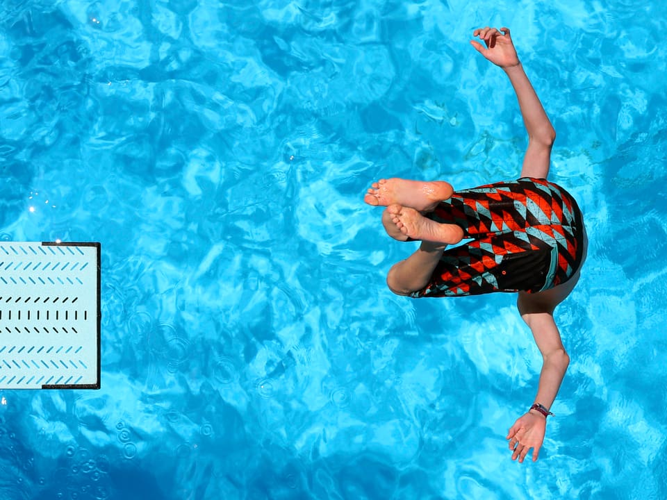 Ein Junge springt von einem Sprungbrett ins Wasser