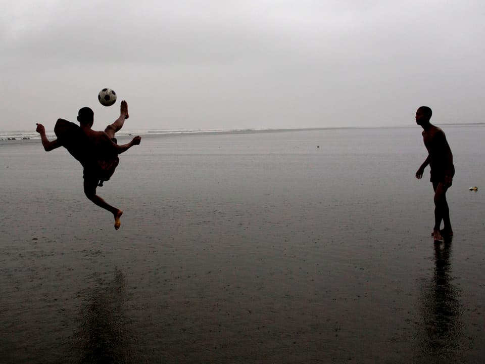 Zwei Männer spielen im Meer Fussball.