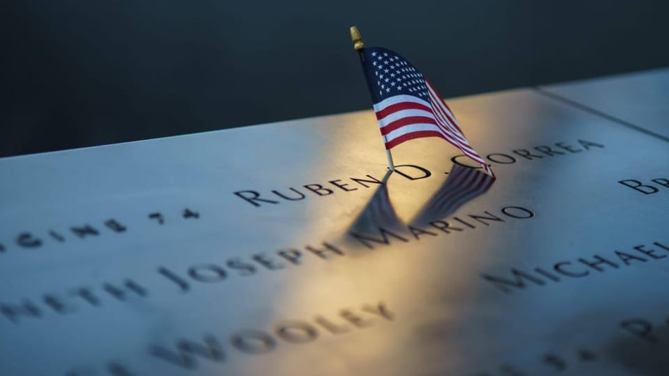 eine US-Flagge steckt im Betonschild mit Namen der Opfer