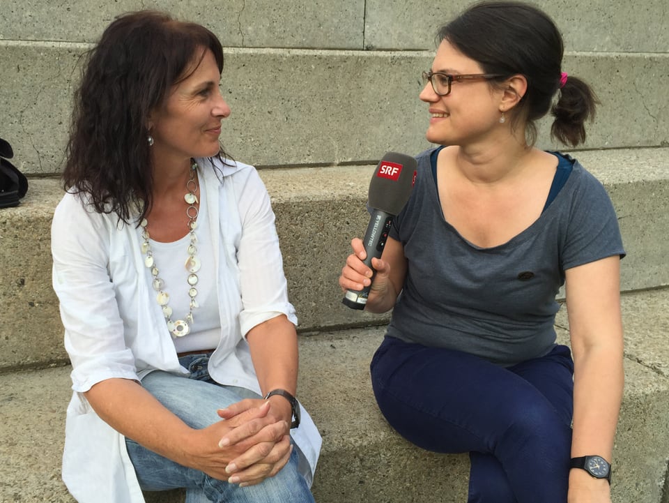 Zwei Frauen auf einer Steintreppe während eines Interviews.