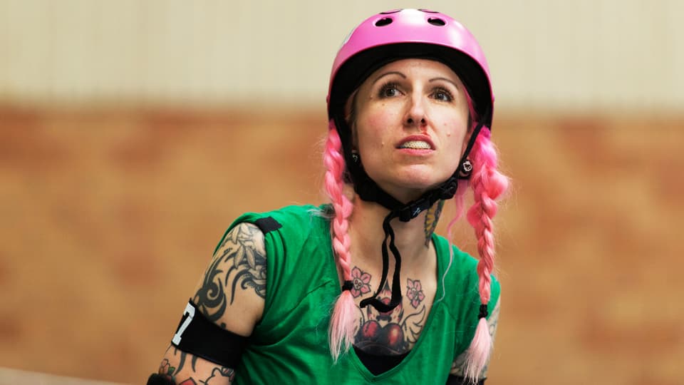 Frau mit rosa Helm und rosa gefärbten Haaren und vielen Tattoos.