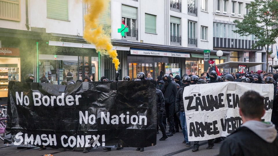 Schwarzvermummte Demonstranten halten ein schwarzes Transparent mit der Aufschirft: «No Border, No Nation. Smash Conex!»