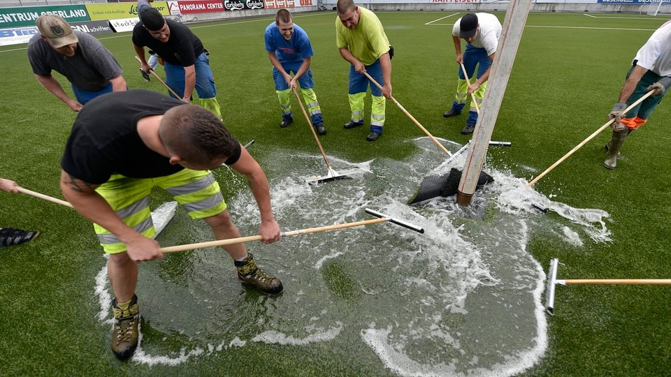 Männer an einer Wasserlache auf einem Fussball-Platz.