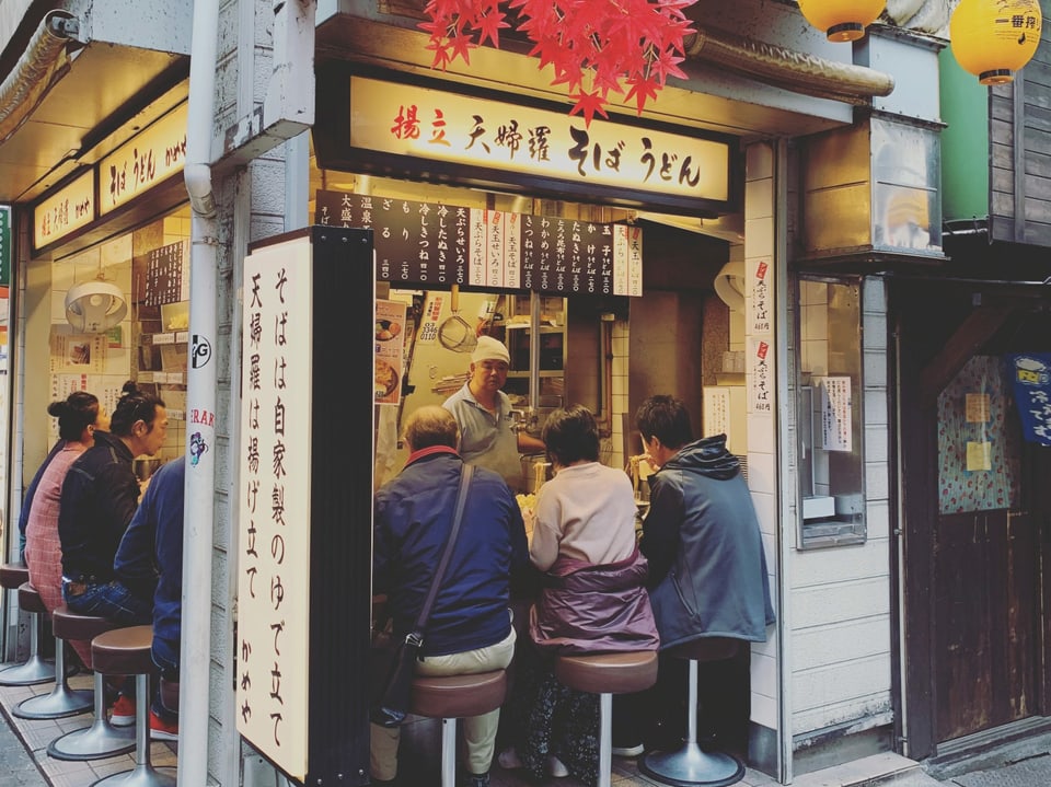 Diverse Leute essen in einem japanischen Nudel-Restaurant schnell eine Schlale Nudeln.