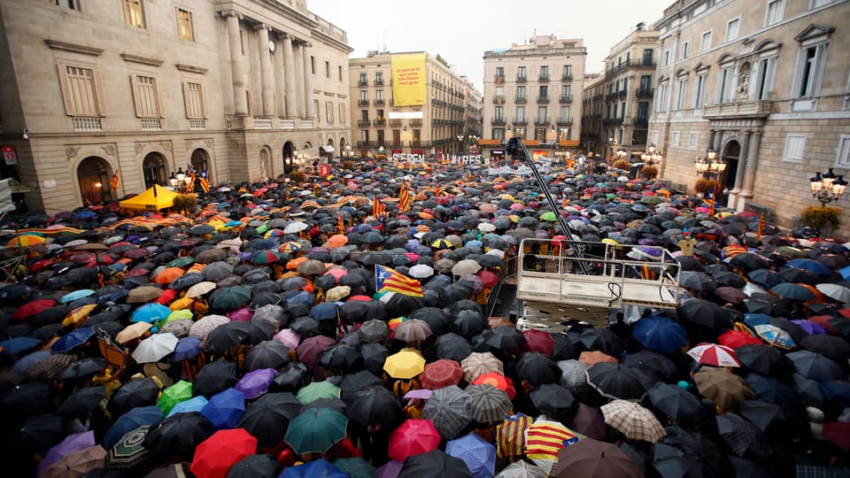 Tausende Menschen stehen unter bunten Regenschirmen auf einem Platz