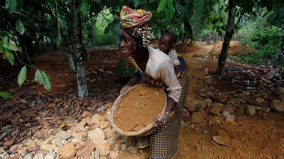 Eine Frau mit Kind trägt Sand, der auf Spuren von Gold untersucht werden soll. 