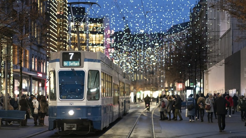 Viele Menschen und ein Tram (7 Bhf. Stettbach) steht unter der Weihnachtsbeleuchtung an der Zürcher Bahnhofstrasse.