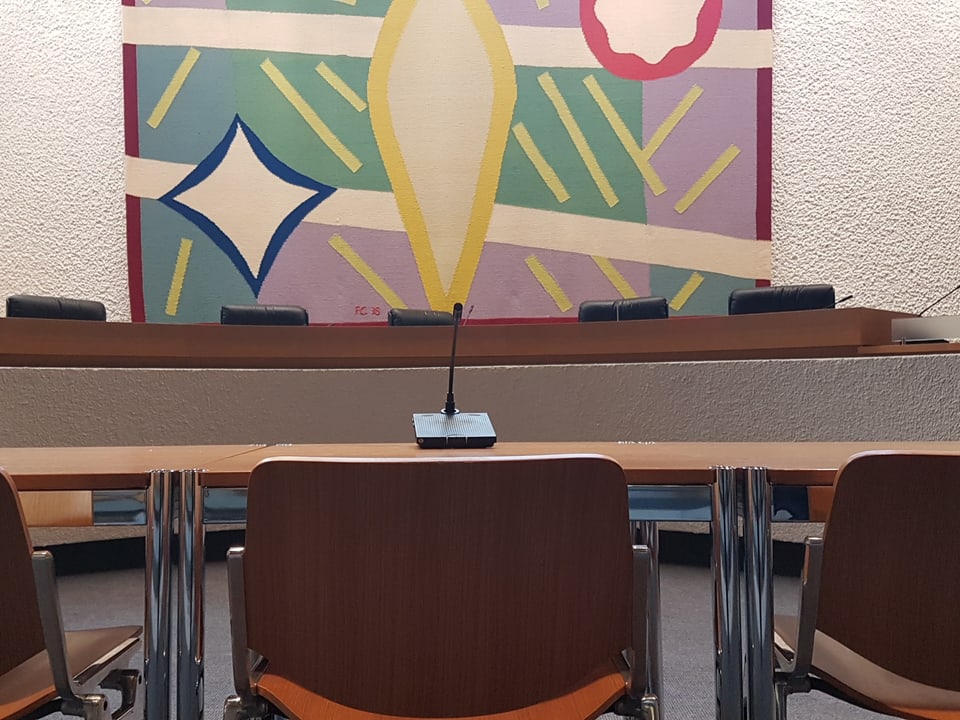 Tisch, Stuhl davor, Teppich im Hintergrund an der Wand