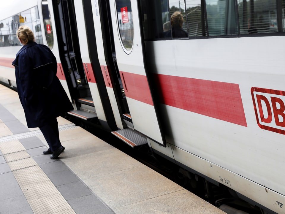 Eine Zugbegleiterin steht neben einer Zugtüre eines DB-Zuges.