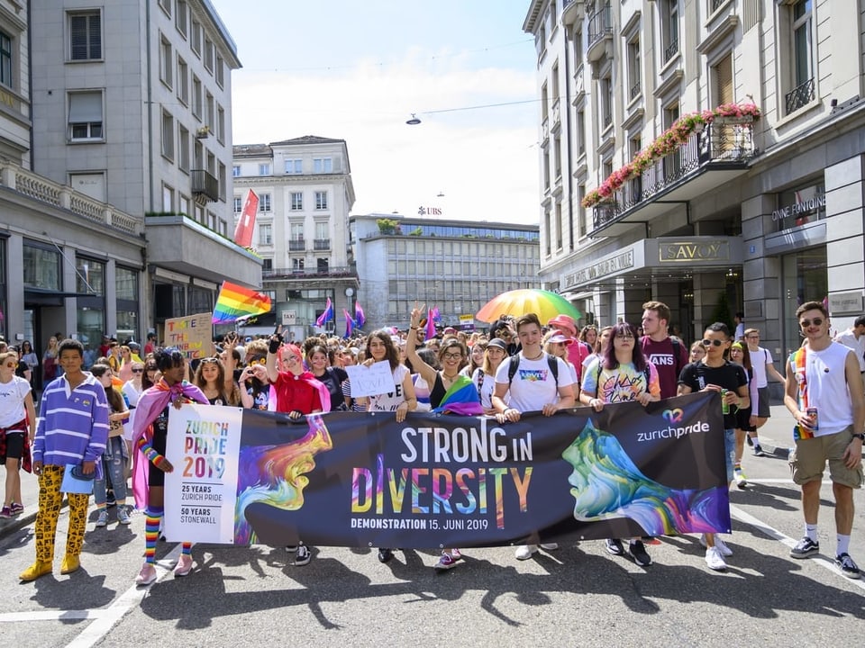 Eine grosse Menschenmenge läuft beim Umzug der Zürich Pride hinter einem grossen Banner mit der Aufschrift «Strong in Diversity».»