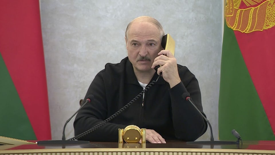 Lukaschenko telefoniert mit einem goldenen Telefon und blickt nachdenklich in die Ferne.